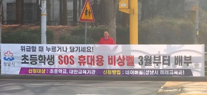 황금석 성남시의원이 초등학교 인근에 설치된 ‘초등학생 SOS 휴대용 비상벨’ 신청 안내 현수막 앞에 서 있다